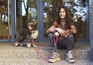 A young woman sits on steps next to a dog with a pink leash, enjoying a sunny day. The scene