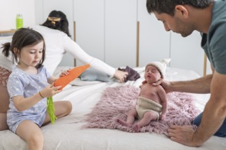 A young family shares tender moments with their newborn baby and big sister. The joyful scene