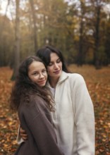 Mother and daughter enjoy a warm embrace amidst the colorful autumn leaves in a serene forest