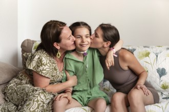 A joyful family moment showing a mother and sister embracing a young girl with a tracheostomy. The