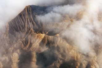 Aerial view of rugged mountain peaks partially covered by mist, creating a dramatic and serene