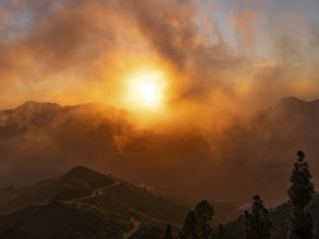 Dramatic sunset lighting up the clouds and mist over the mountains, viewed from Cruz de Tejeda in
