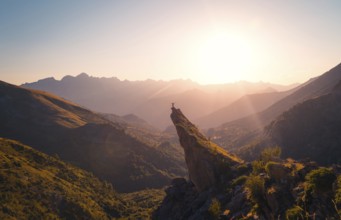 A breathtaking view of a hiker standing on a mountain peak, bathed in the golden light of a sunrise