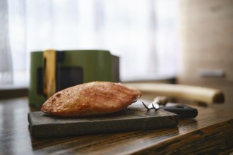 Roasted pork fillet rests on a wooden cutting board in a kitchen table. Air fryer basket and