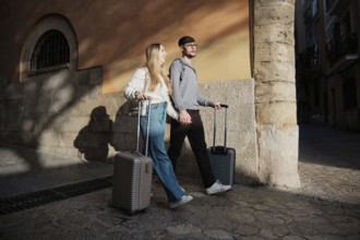 A young couple strolls through a picturesque street in Majorca, Spain. They hold hands and pull