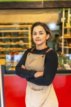 Vertical photo of a latin confident woman worker wearing apron standing proud in a bakery shop