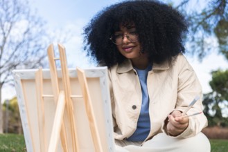 A young black woman enjoys painting outdoors in a sunny park, capturing the beauty of nature. She
