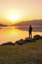 Lonely person standing at the lakeside and watching the sunset, Großer Alpsee, Immenstadt im