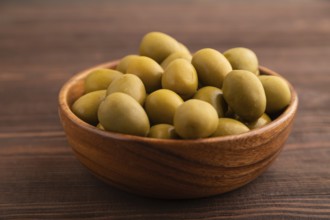 Fresh green olives in wooden bowl on brown wooden background. side view, close up, selective focus