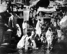 Au pied des Ghats de Bénarès, groupe de femmes prenant leur bain rituel dans le Gange (1929)
