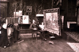François Flameng in his studio, sitting next to one of his paintings (1903)