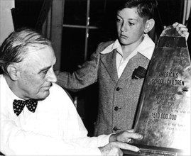 President Roosevelt examining a piece of propeller of a Japanese plane shot down, on which is written the financial participation of school children during the war. The school children's delegate is D...