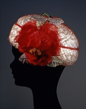 White cellophane hat covered with red veil and chiffon flower decoration with printed velvet leaves
