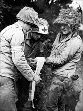 Deux ambulanciers du corps médical américain traitent un blessé dans la région de St-Lo en Normandie. (France, été 1944)