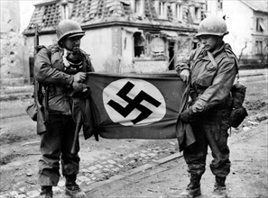 Deux soldats américains montrent un drapeau nazi trouvé à Haguenau (France), le 10 décembre 1944.