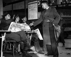 Des soldats américains aident une vendeuse de journaux à vendre une édition spéciale de la presse parisienne. (10 août 1945)