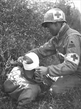 Un membre du corps médical US bande la tête d'un soldat blessé près de Bremencourt en France. 12 septembre 1944