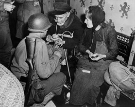 Des soldats américains offrent du chocolat à des civils français à La Haye du Puits. 
(Eté 1944)