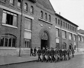 A Reims, des prisonniers de guerre allemands passent devant un établissement scolaire.
(23 mai 1945)