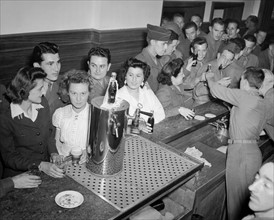 Soldats américains, membres du  corps d'armée féminin et jeunes Françaises se désaltèrent en buvant du coca-cola et de la bière au camp de Suippes
(Juillet 1945)