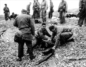 Des soldats américains apportent leur aide à un camarade sur une plage de Normandie. (20 juin 1944)