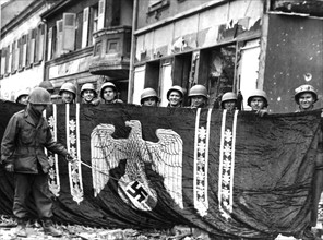 Soldats américains exhibant le drapeau nazi réquisitionné à Buss, en Allemagne. (20 mars 1945)