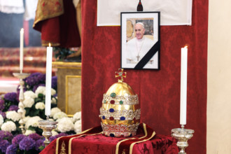 Eine Papstkrone, die sogenannte Tiara, liegt vor einem Bild vom verstorbenen Papst. Zu Ehren des