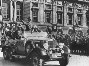 Adolf Hitler grüßt die ihm zujubelnde Menschenmenge in Wien stehend in einem Auto, sitzend neben