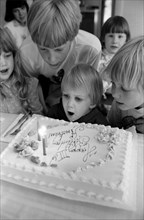 Young Boy Blowing out Birthday Cake Candles as Other Children Watch