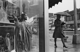 Women Walking with Umbrella and Jesus Statue in Store Window