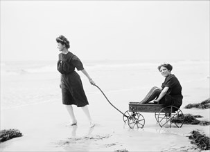Woman Pulling another Woman in Wagon on Beach, USA, Detroit Publishing Company, 1905