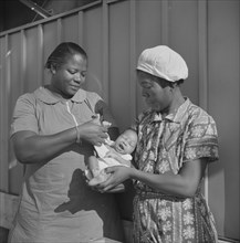 Nurse Examining Infant with Mother and Child Receiving Prenatal and Postnatal Care, Okeechobee Migratory Labor Camp, Belle Glade, Florida, USA, Marion Post Wolcott for Farm Security Administration, Ju...