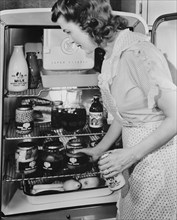 Woman at Refrigerator filled with Food Products in Glass Jars due to Restriction of Metal Products because of Military Needs during World War II, USA, Office of War Information, January 1943