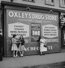 Two High School Girls and Woman Standing in front of Large Store Sign, Southington, Connecticut, USA, Fenno Jacobs for Office of War Information, May 1942