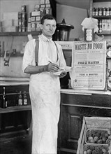 Grocery Store Worker Standing next to Sign "Waste No Food!", Harris & Ewing, 1917