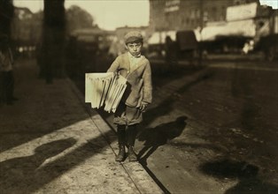 Young Newsboy, (thinks he is) 8 years old, Works Until 6:30 p.m. Every Night, Full-Length Portrait Selling Newspapers on Street, Northampton, Massachusetts, USA, Lewis Hine for National Child Labor Co...
