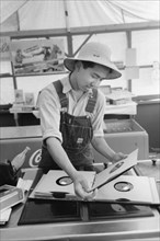 Japanese-American Farm Worker from the Farm Security Administration (FSA) Mobile Camp Selecting a Gramophone Record in Recreation Tent, Nyssa, Oregon, USA, Russell Lee, Farm Security Administration, J...