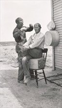 Man Cutting another Man's Hair as he's Seated on Box and Chair Outdoor, Idaho, USA, by Otto M. Jones, 1910's