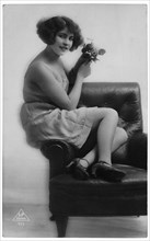 French Lingerie Model Seated on Arm of Chair Holding Flowers, circa 1920