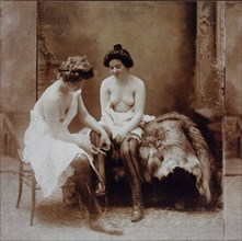 Two Partially Nude Women, One Woman is Measuring the Other Woman's Calf with Tape Measure, circa 1900
