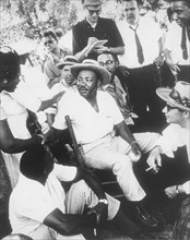 Martin Luther King, Jr in Straw Hat Sitting Down with Group of Men While Shaking Hands with Woman, circa 1960's