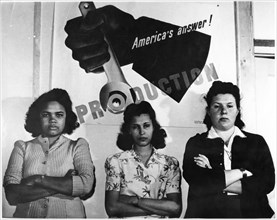 Three Female Factory Workers Standing in Front of "America's Answer! Production" Poster during World War II, circa 1943, from the Documentary Film, "The Emerging Woman", Women's Film Project, 1974