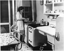 Woman Cooking in Kitchen with Young Boy Eating Cookies with Milk, USA, circa 1955, from the Documentary Film, "Emerging Woman", Women's Film Project, 1974