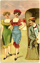 Man in Wicker Chair Staring at Two Fashionable Women in One-Piece Bathing Suits Strolling Along Beach, Postcard, circa early 1900's