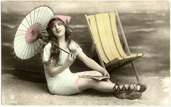 Seated Woman in Blue Swim Dress Holding Parasol next to Beach Chair, circa early 1900's