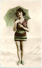 Woman in Brown Swimsuit, Striped Parasol and Green Striped Shoe Standing on Beach,  Hand-Colored, Postcard, circa early 1900's