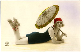 Smiling Woman in Green Swimsuit and Red Swim Cap Laying Down while Holding Parasol, Portrait, Hand-Colored French Postcard, circa early 1900's