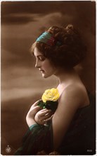 Woman in Green Dress and Headband Holding Yellow Rose against Chest, Profile, Hand-Colored Postcard. Circa 1920's