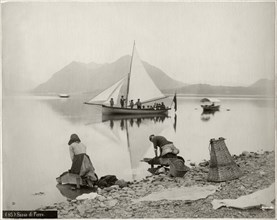 Two Women Doing Laundry at Shore of Lake Maggiore with Sailboat and Sasso di Ferro Mountain in Background, Lombardy, Italy, circa 1880