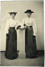 Portrait of Two Adult Women in Hats and Long Dresses Leaning on Pillar, circa 1870